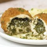 Close-up of Chicken Kiev being sliced open, showing melted garlic herb butter spilling from the center.