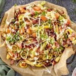 Overhead view of loaded dirty fries with bacon, banana peppers, fresh tomatoes, green onions, and mayonnaise drizzle.