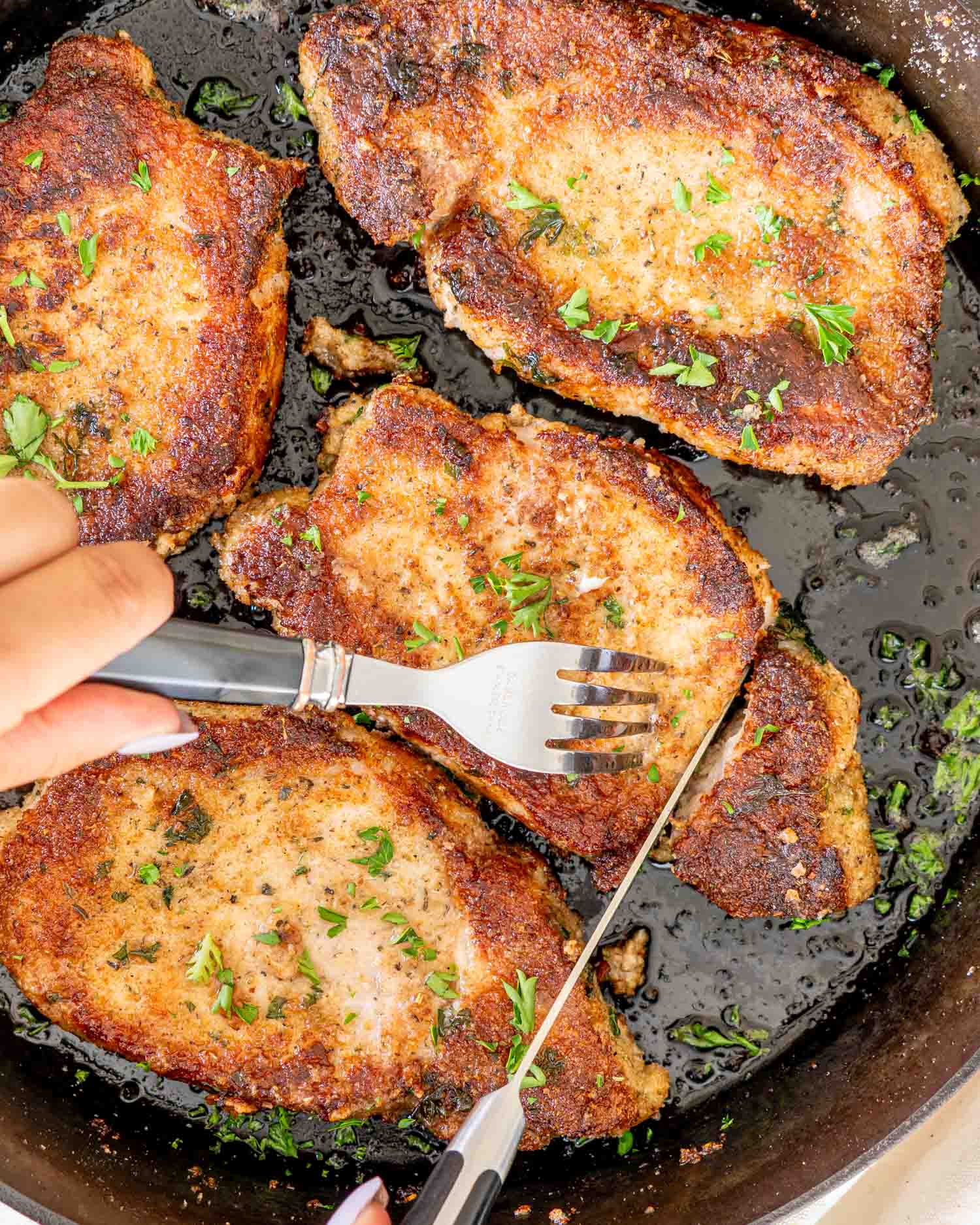 italian breaded pork chops in a cast iron skillet garnished with some parsley.