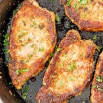 italian breaded pork chops in a cast iron skillet garnished with some parsley.