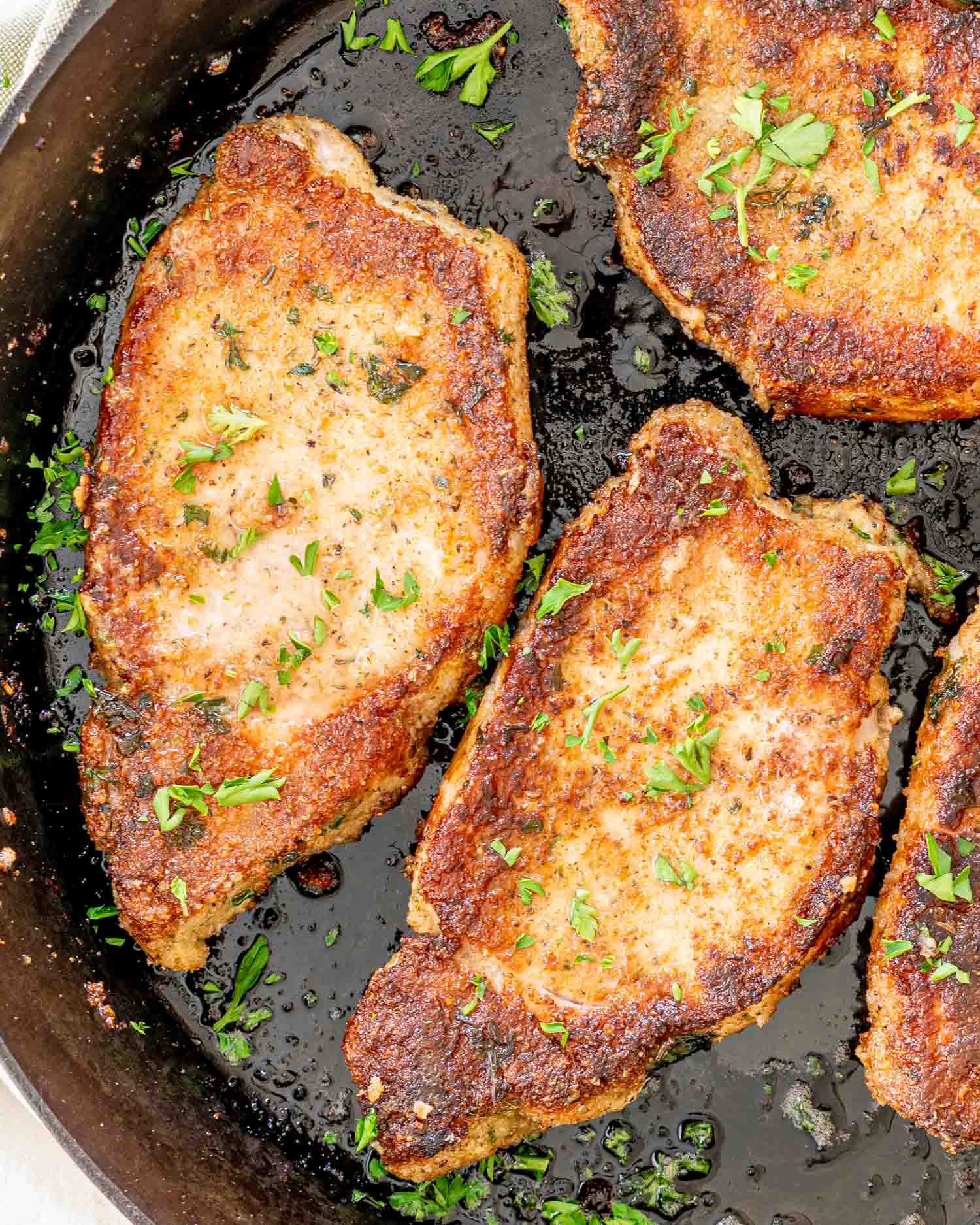 italian breaded pork chops in a cast iron skillet garnished with some parsley.