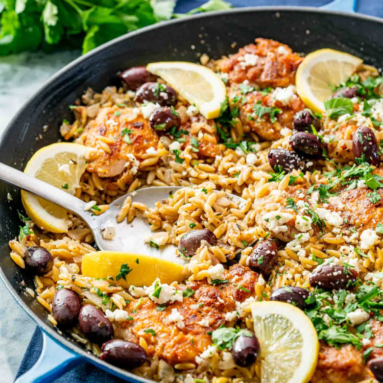 one pot greek chicken orzo in a skillet garnished with lemon wedges and parsley.