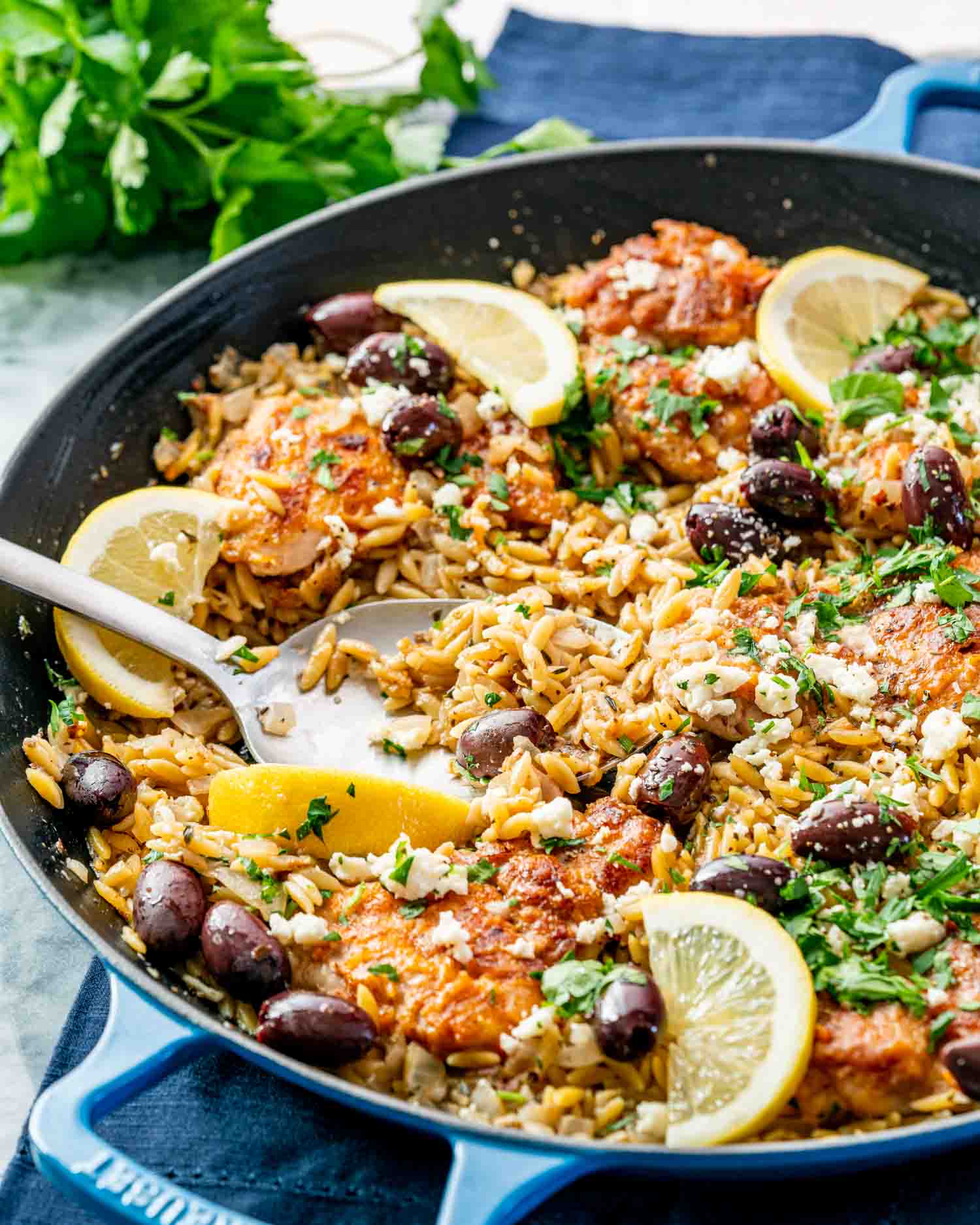one pot greek chicken orzo in a skillet garnished with lemon wedges and parsley.