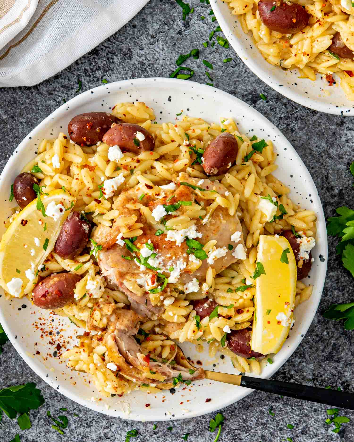 a serving of greek chicken orzo on a white plate garnished with feta cheese and parsley.