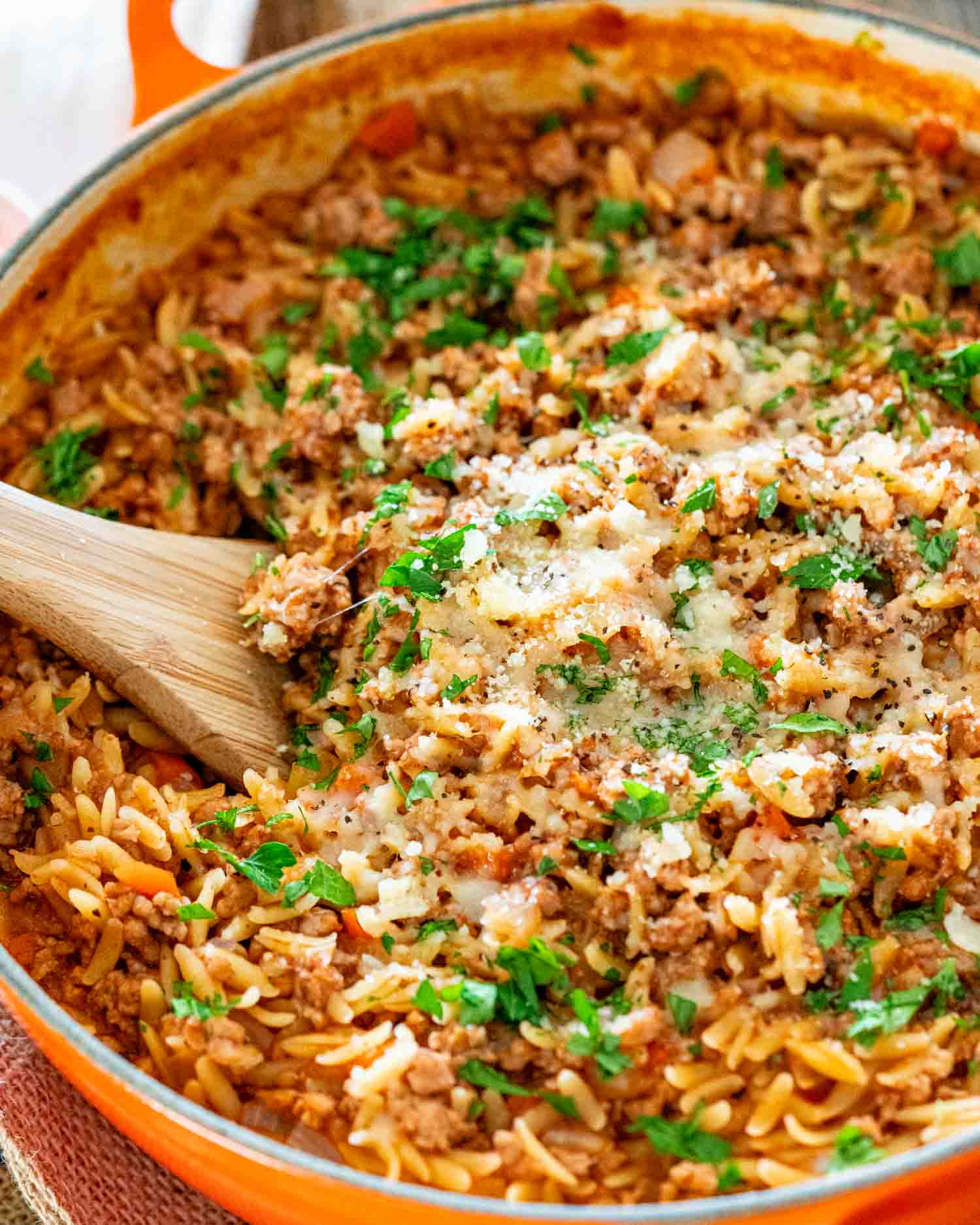 spicy pork ragu orzo garnished with parmesan and parsley in a skillet.