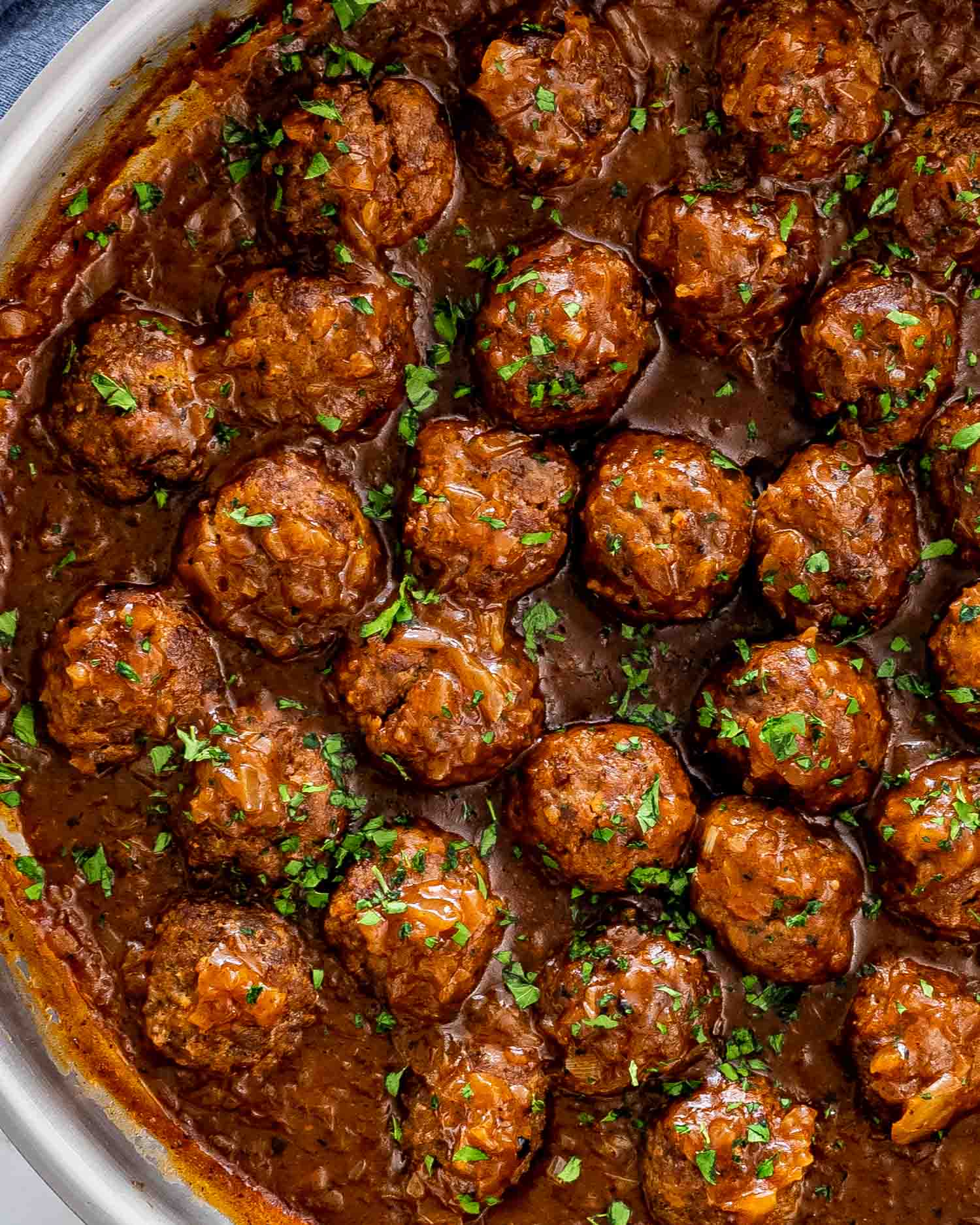 salisbury steak meatballs with gravy in a skillet garnished with parsley.