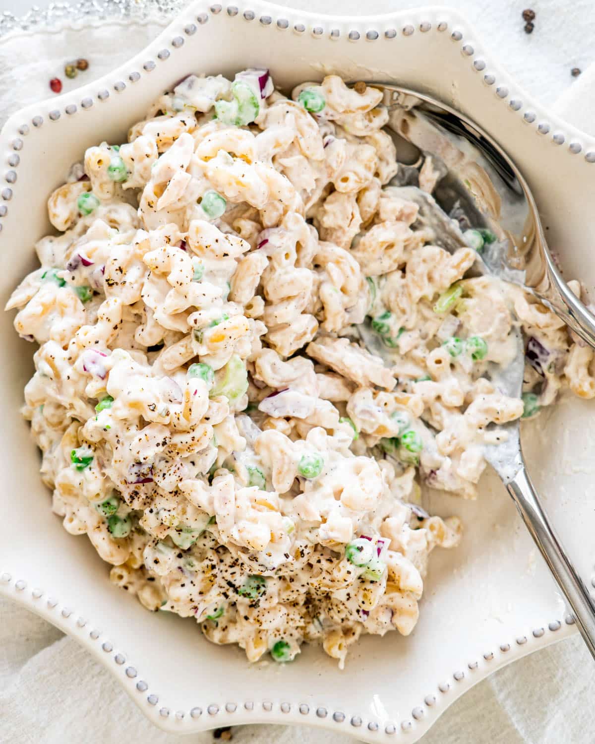 a white bowl loaded with macaroni salad with two serving spoons