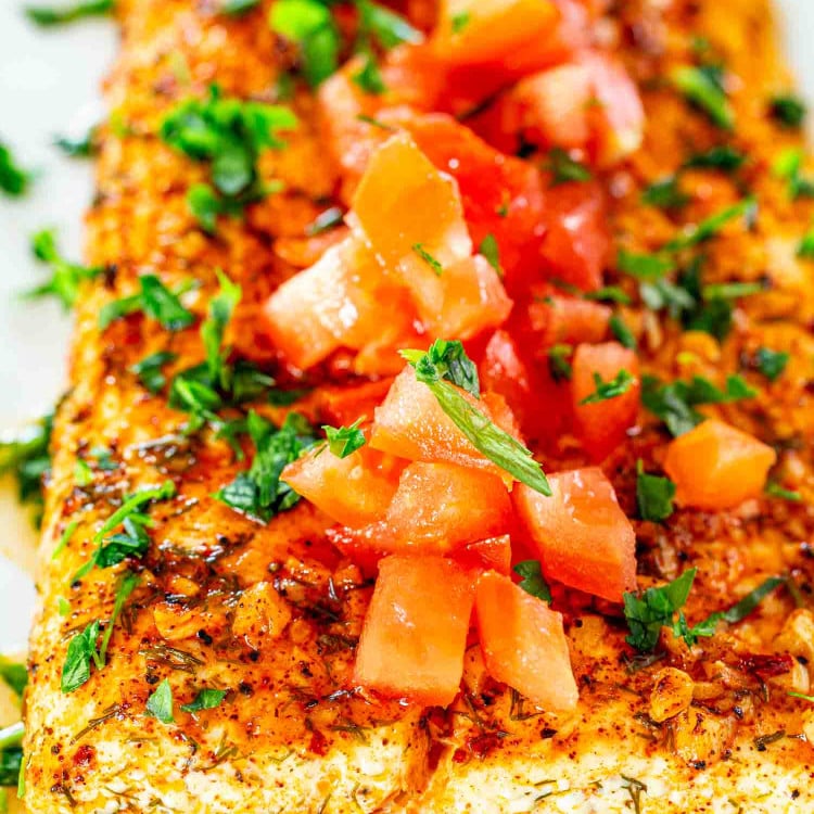 baked lemon garlic halibut filet topped with tomatoes on a white dish.