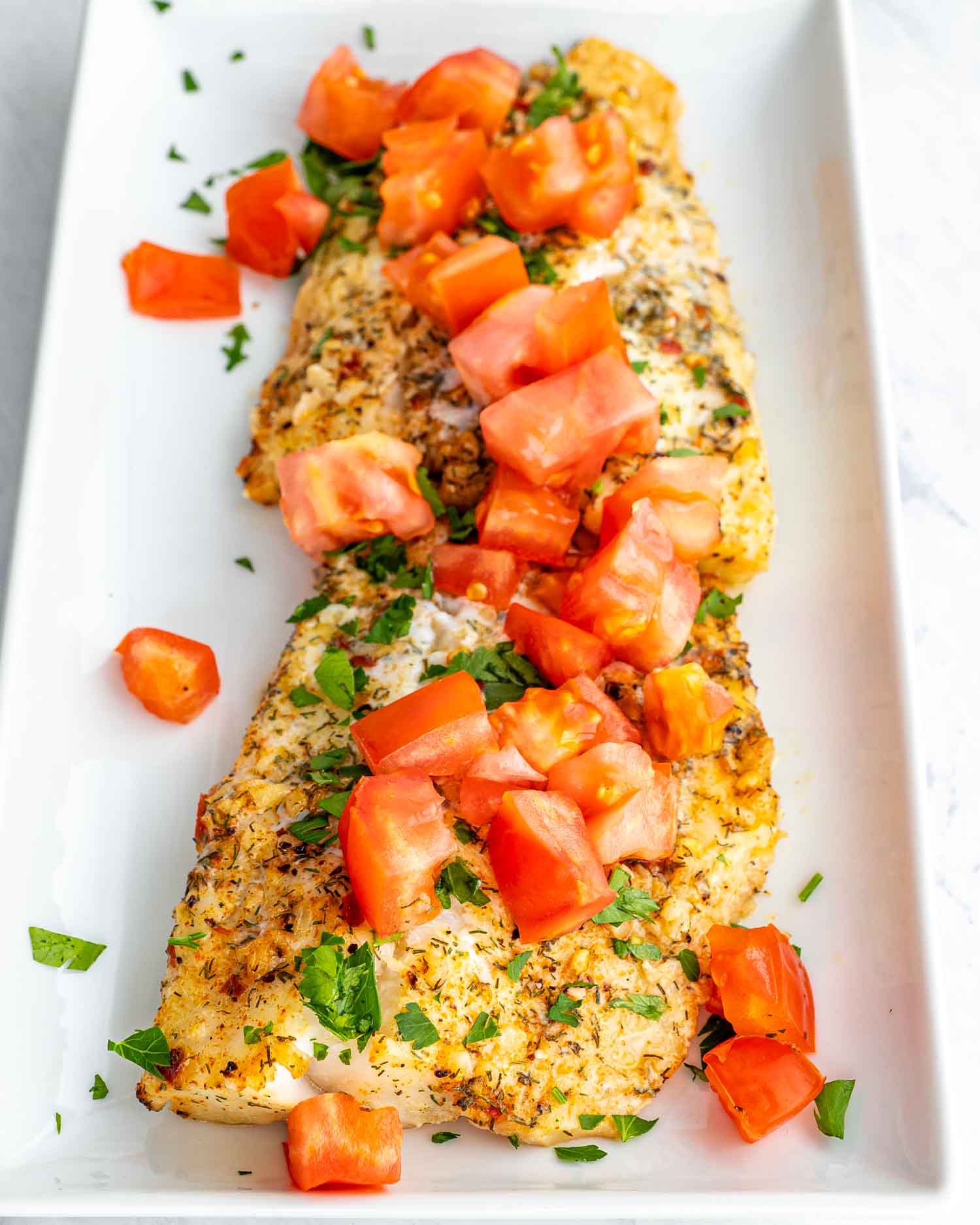 baked lemon garlic halibut filet topped with tomatoes on a white dish.