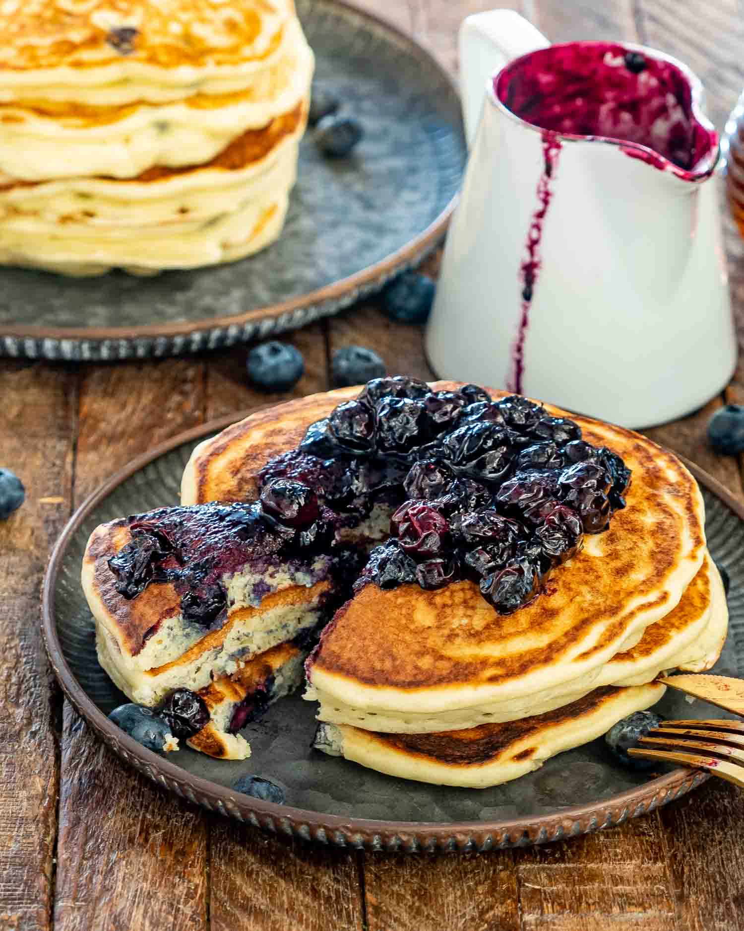 blueberry buttermilk pancakes with a wedge cut out of them on a plate with blueberry sauce.