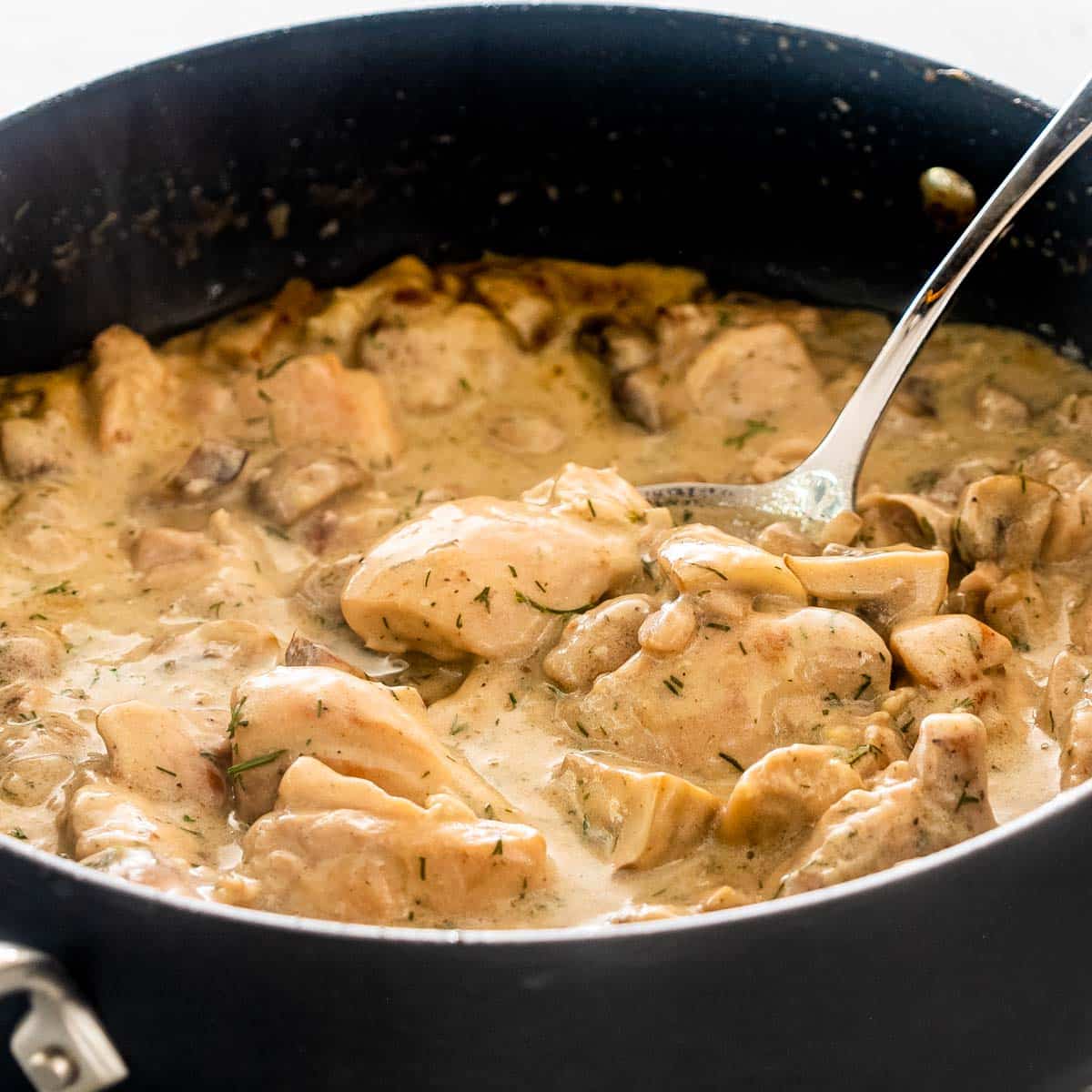 chicken and mushrooms in creamy dill sauce in a black skillet with a serving spoon inside.