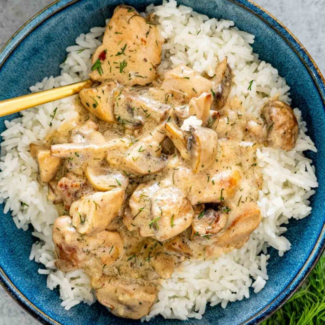chicken and mushroom in creamy dill sauce over a bed of rice in a blue bowl.