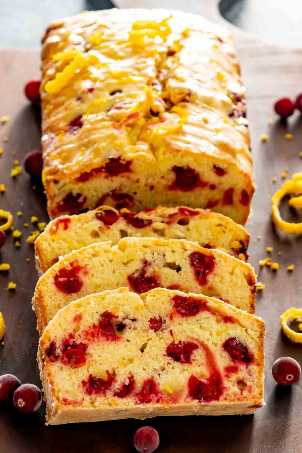 a cranberry orange bread with a few slices cut out of it on a cutting board.