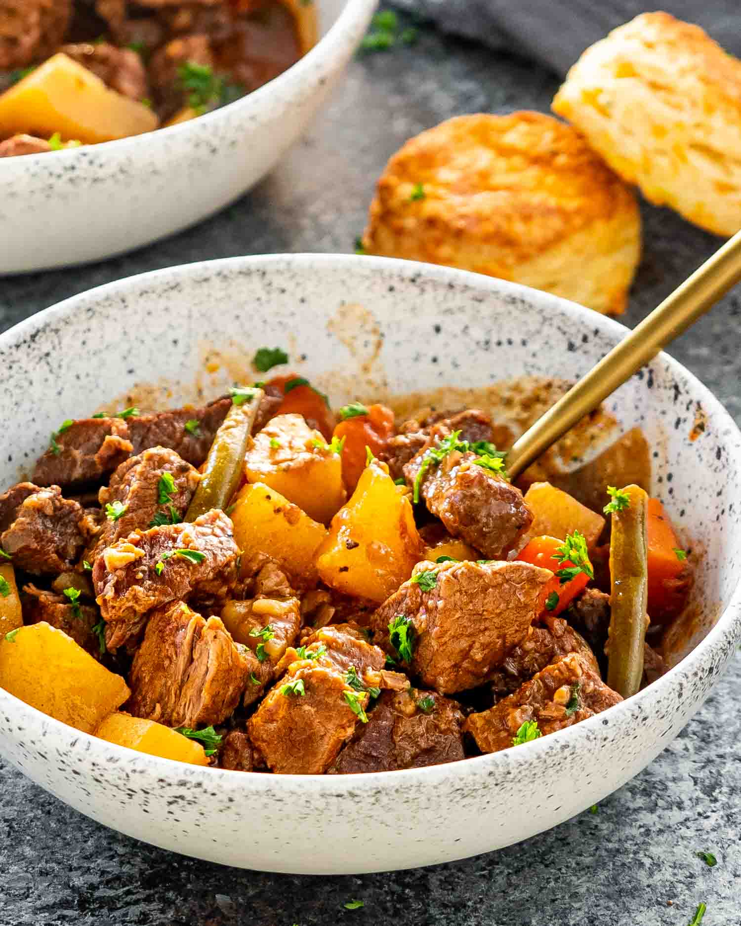 a serving of beef stew in a white bowl with a gold fork.