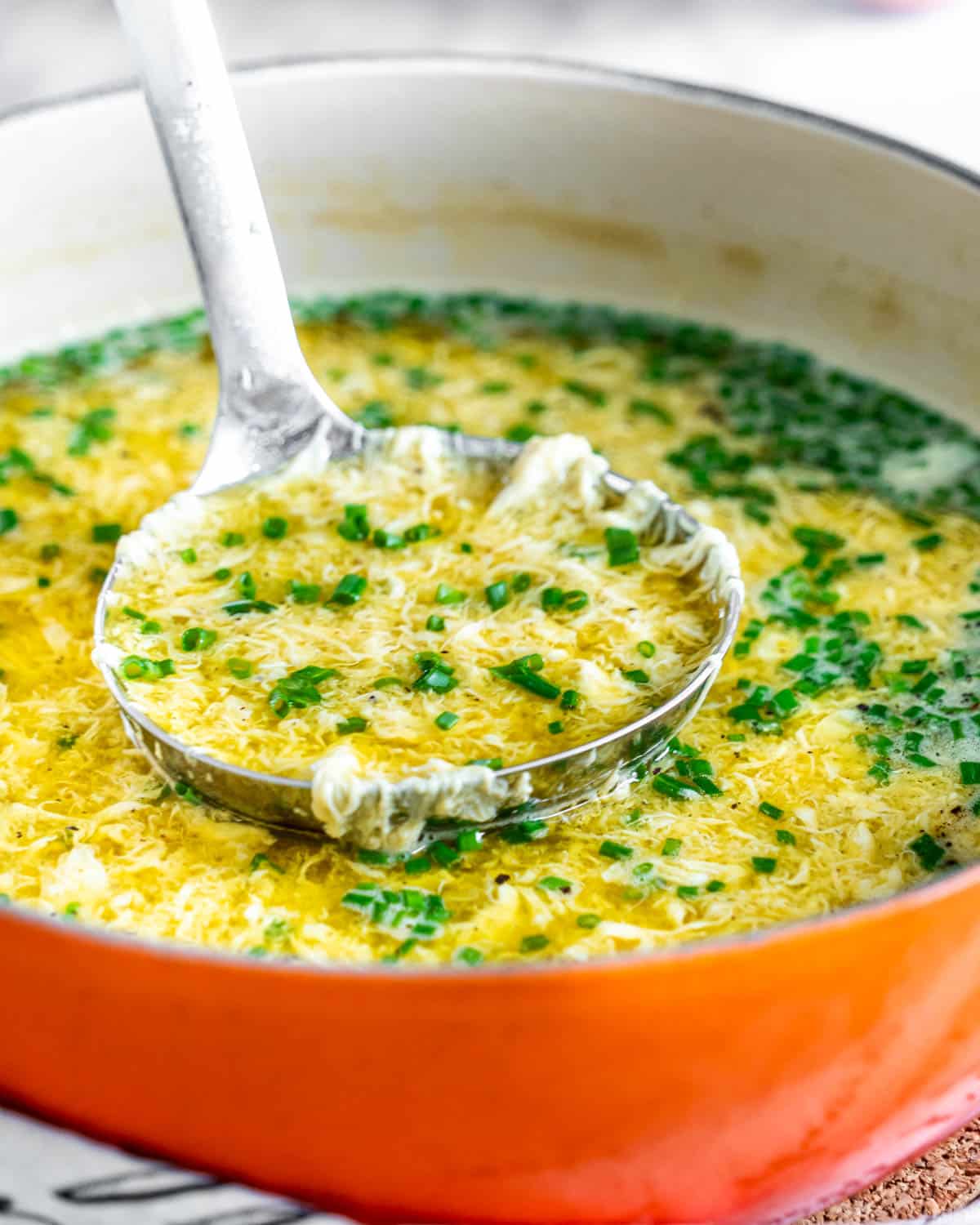 dutch oven filled with soup and a ladle holding some soup that's garnished with chives