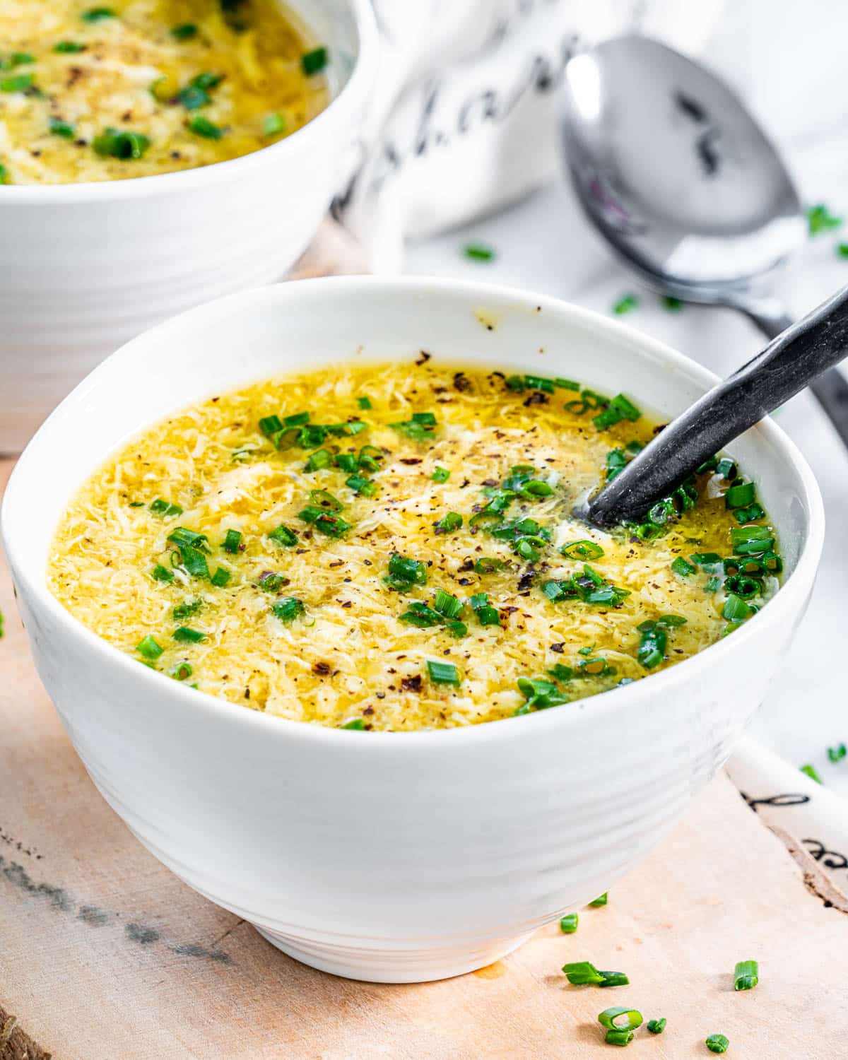 two bowls filled with egg drop soup on a small cutting board and garnished with chives
