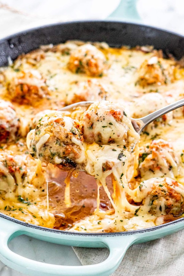 a spoon holding up two french onion meatballs from the skillet
