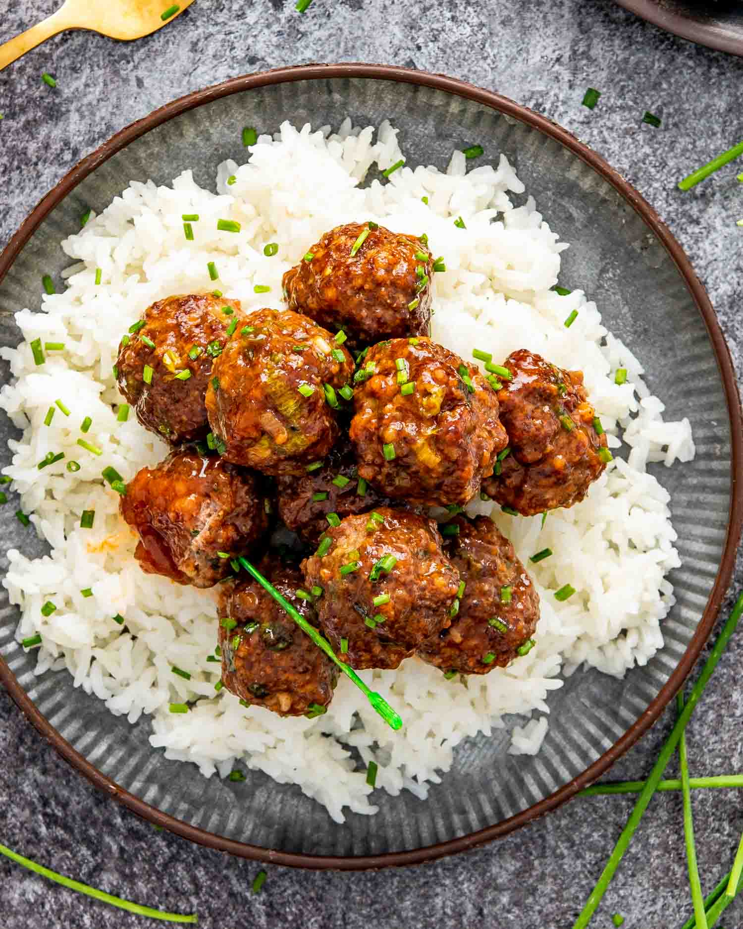korean meatballs on a metal plate on a bed of rice garnished with chives.
