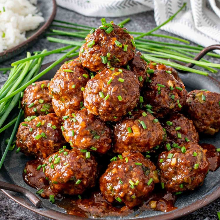 korean meatballs on a metal plate garnished with chives.