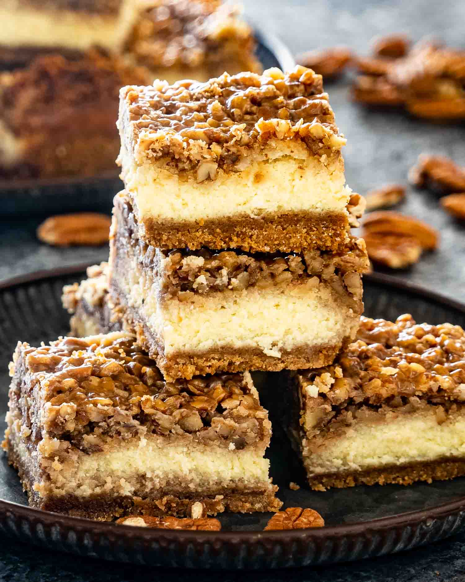 a few pecan pie cheesecake bars stacked on a plate.