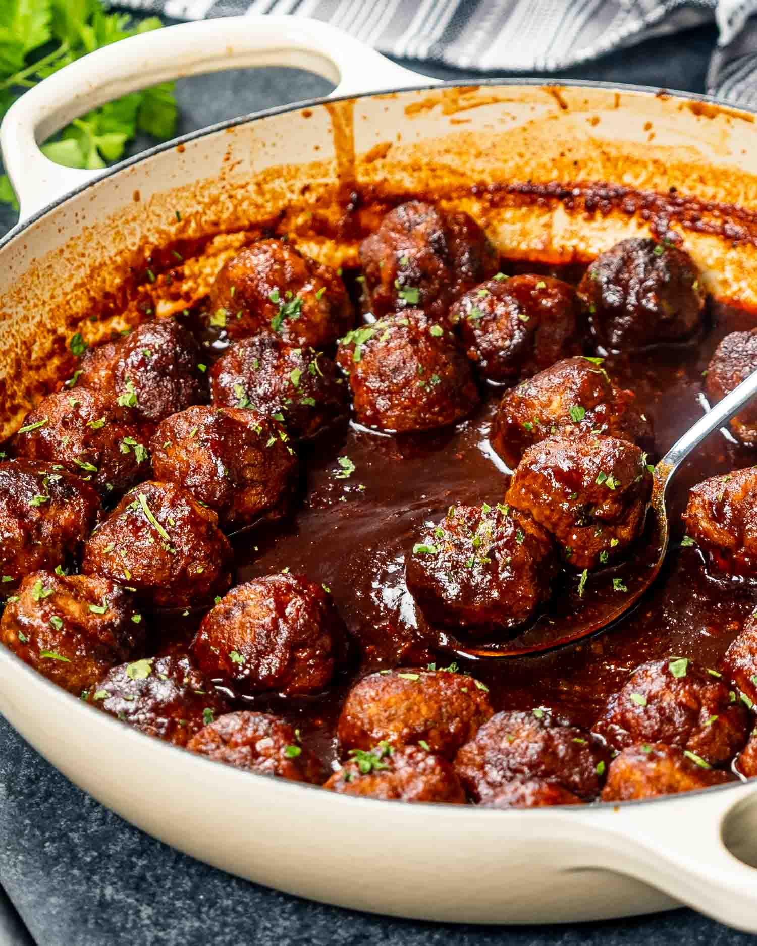 Savory stout meatballs, beautifully browned and simmering in a rich, smoky stout-infused BBQ sauce, served in a beige braiser, garnished with fresh parsley.