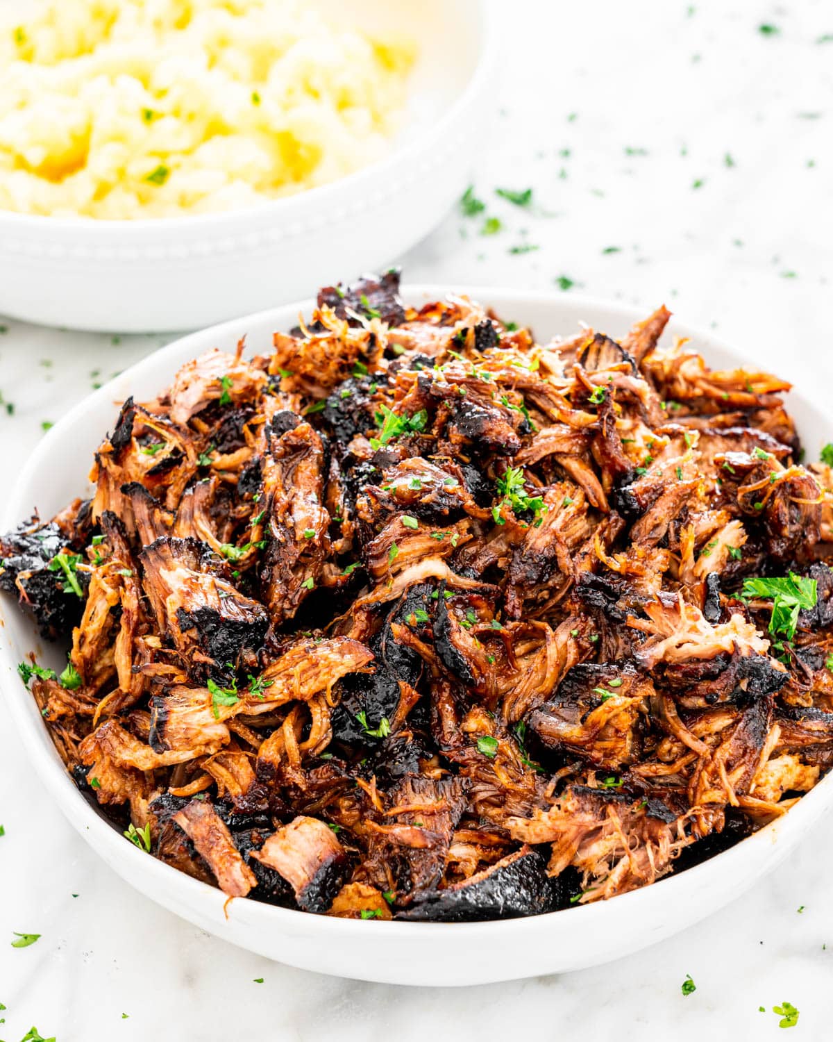Brown Sugar Balsamic Pulled Pork in a white bowl with a bowl of mashed potatoes in the background