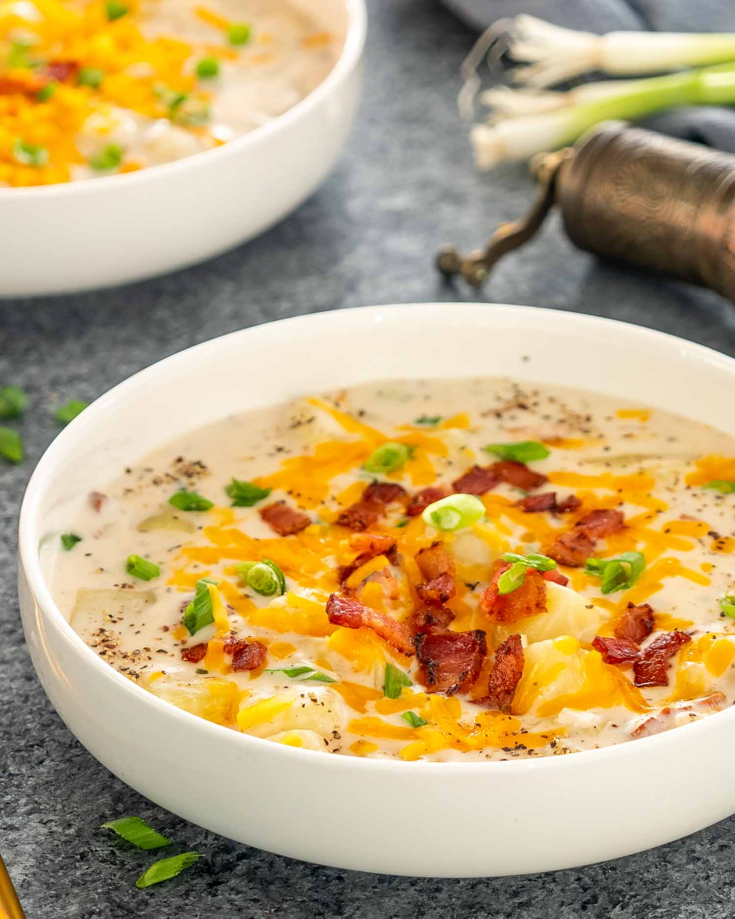 a white bowl full of creamy potato soup garnished with cheddar cheese, bacon and green onions.