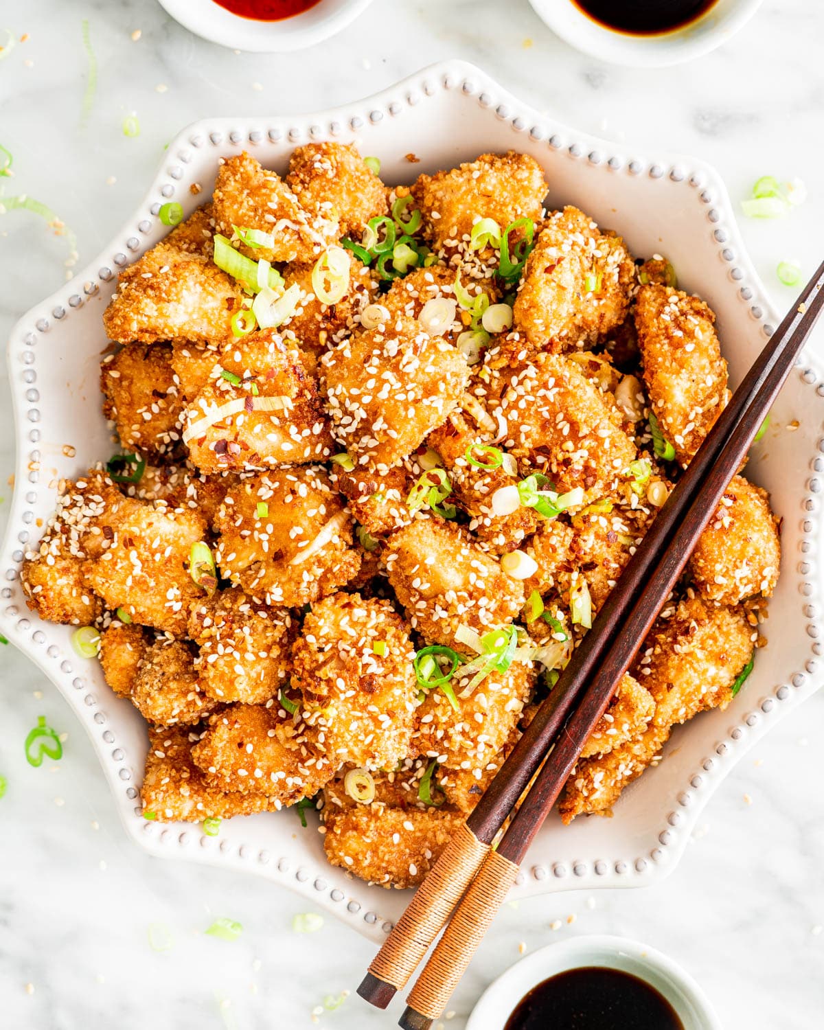 overhead shot of a white bowl loaded with Honey Sesame Chicken with 2 chopsticks on top