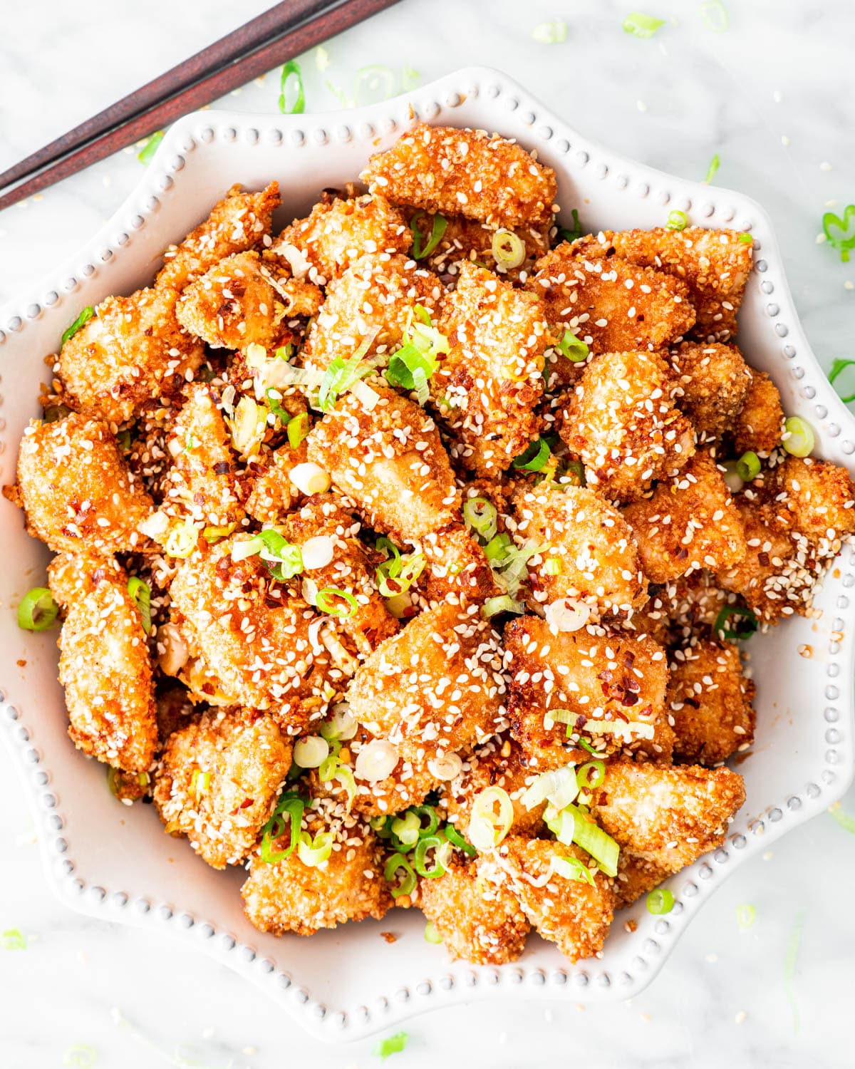 overhead shot of a bowl loaded with honey sesame chicken garnished with green onions