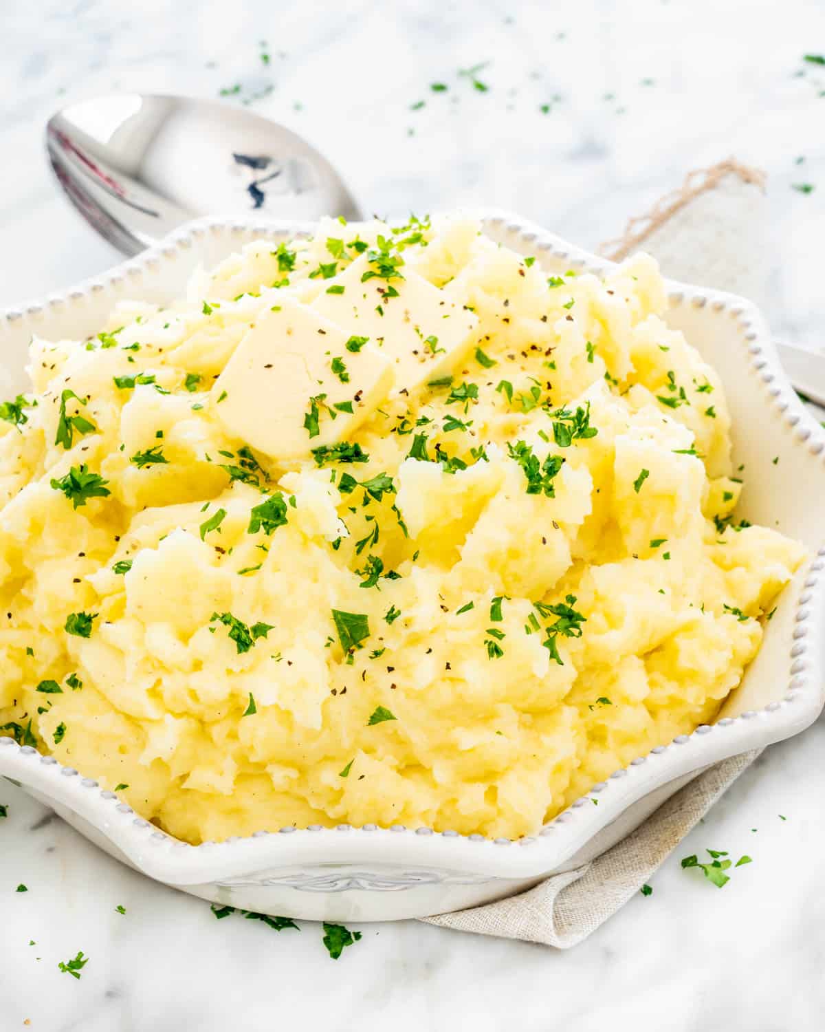 mashed potatoes in a white bowl with some butter over top and garnished with parsley