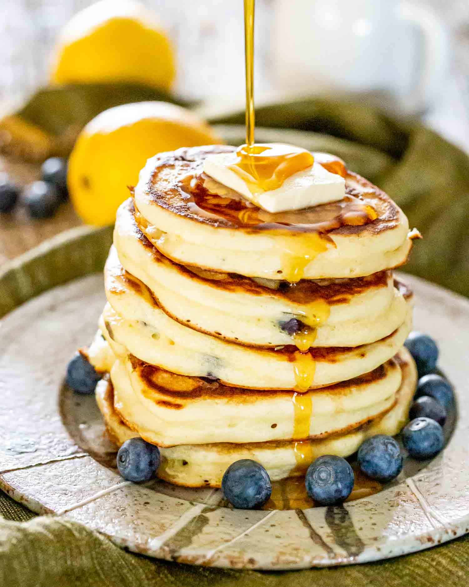 drizzling of maple syrup  over a stack of lemon blueberry ricotta pancakes.
