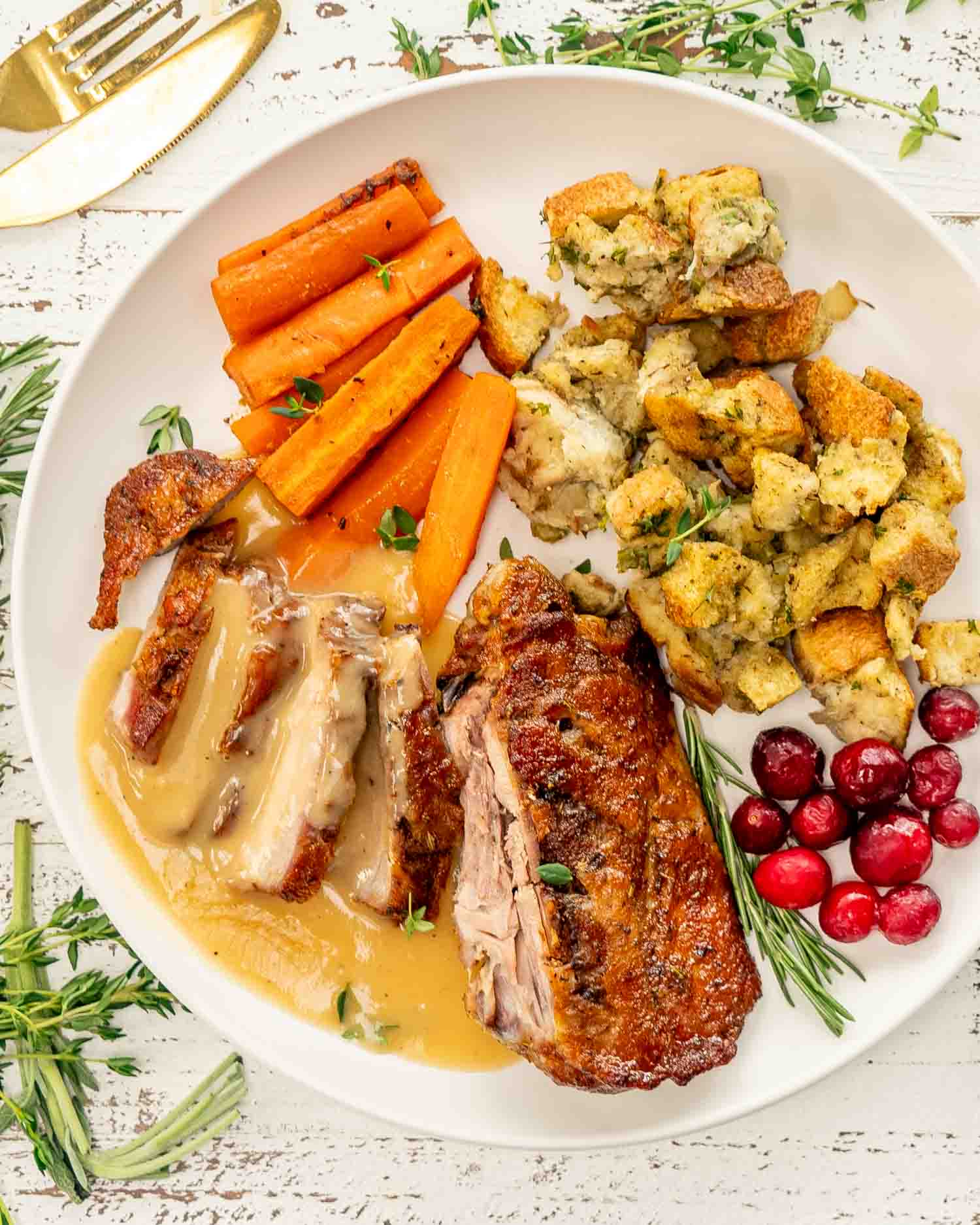 a maple mustard roasted turkey thigh sliced on a white plate along some stuffing and roasted carrots.