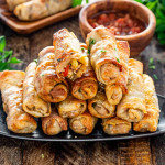 a few egg rolls stacked on a black plate.