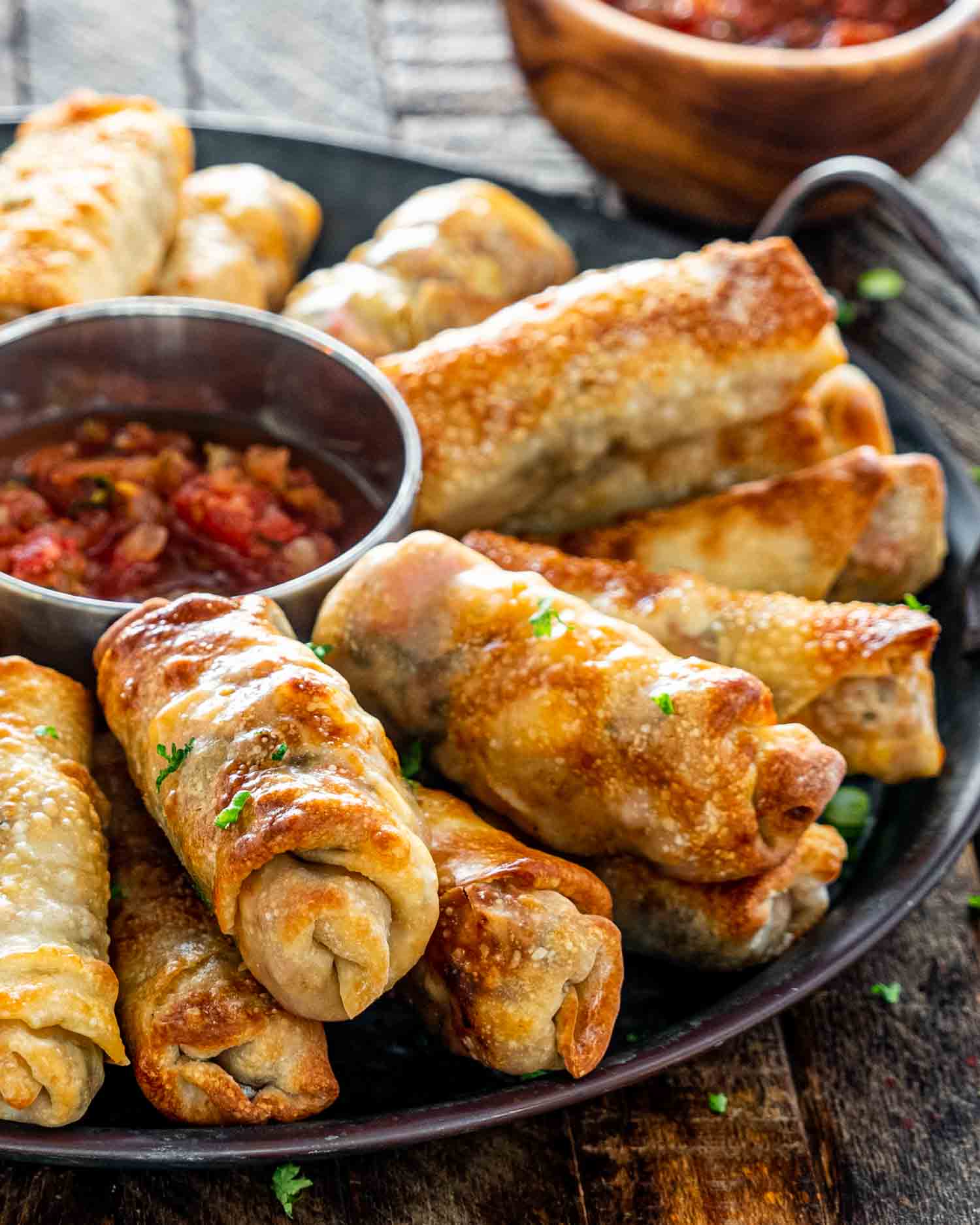 egg rolls on a metal platter with a bowl with salsa in the middle.