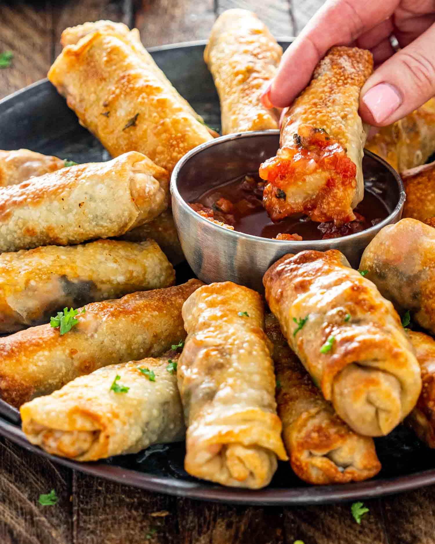 egg rolls on a metal platter with a bowl with salsa in the middle.