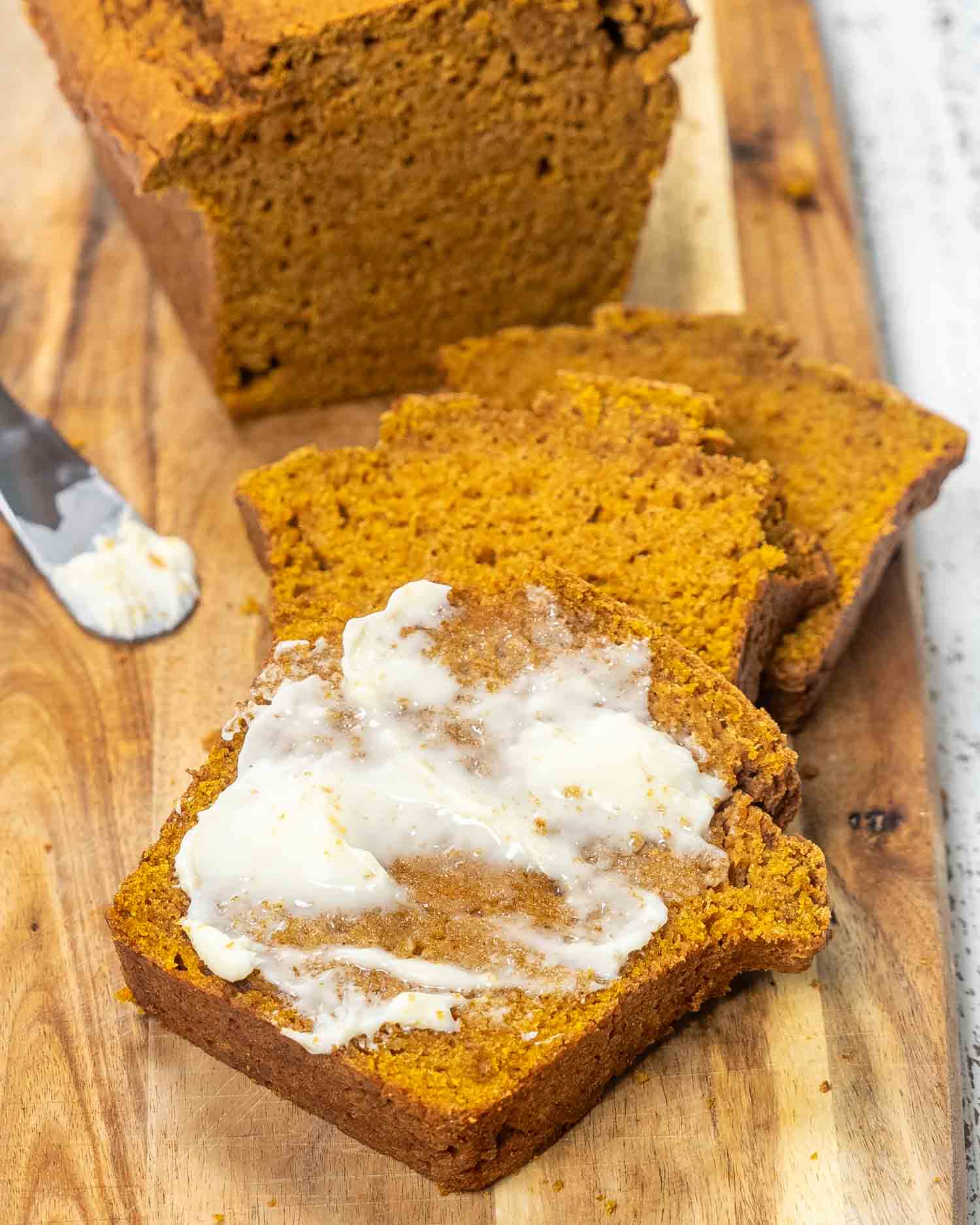a few slices of pumpkin bread on a cutting board, one of them spread with butter.
