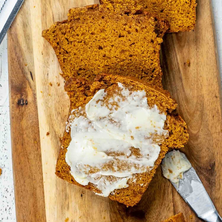 a few slices of pumpkin bread on a cutting board, one of them spread with butter.