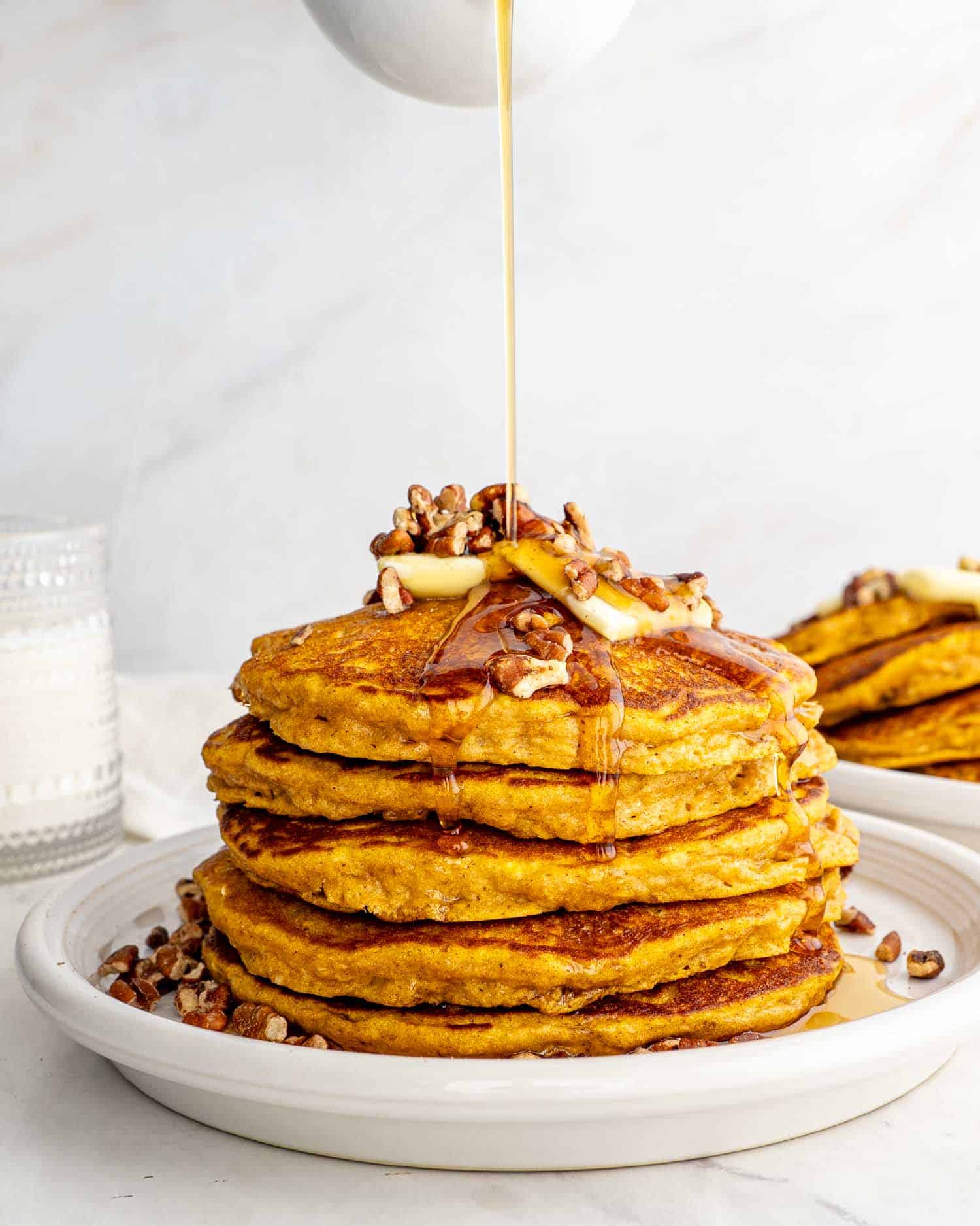 stack of whole wheat pumpkin pancakes on a white plate with pecans and a pat of butter.