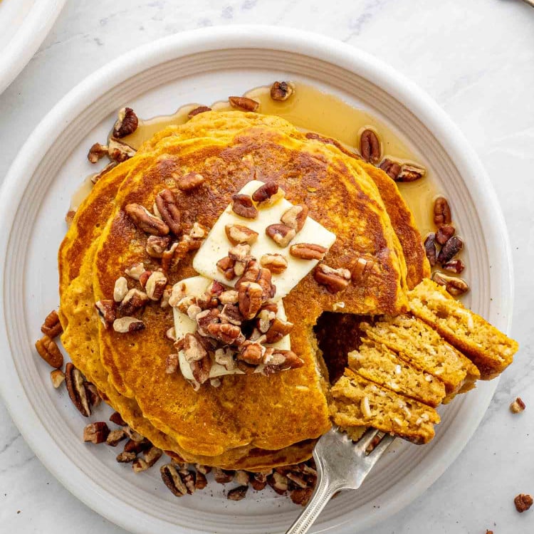 Stack of whole wheat pumpkin pancakes on a plate with a fork taking a piece.