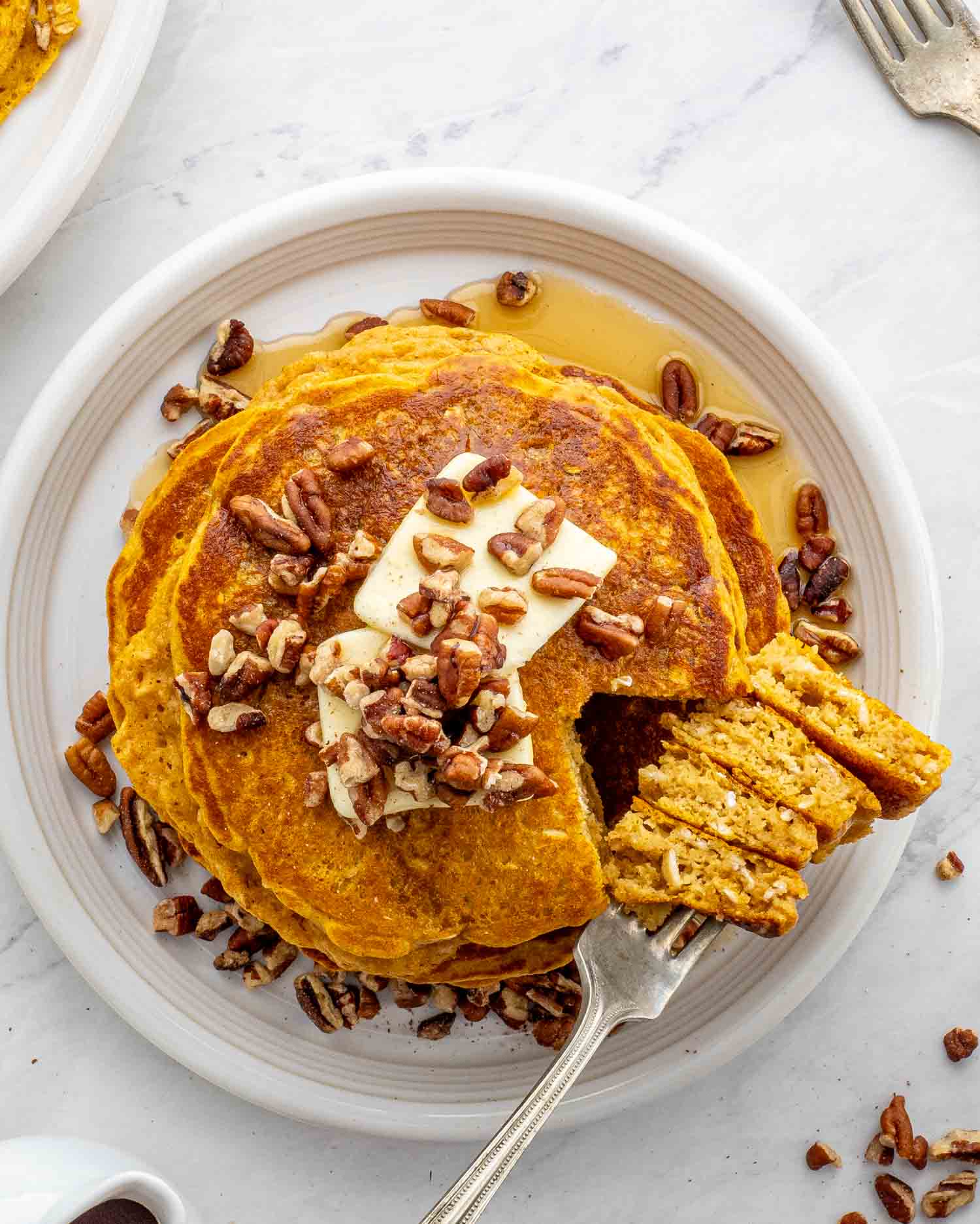 Stack of whole wheat pumpkin pancakes on a plate with a fork taking a piece.