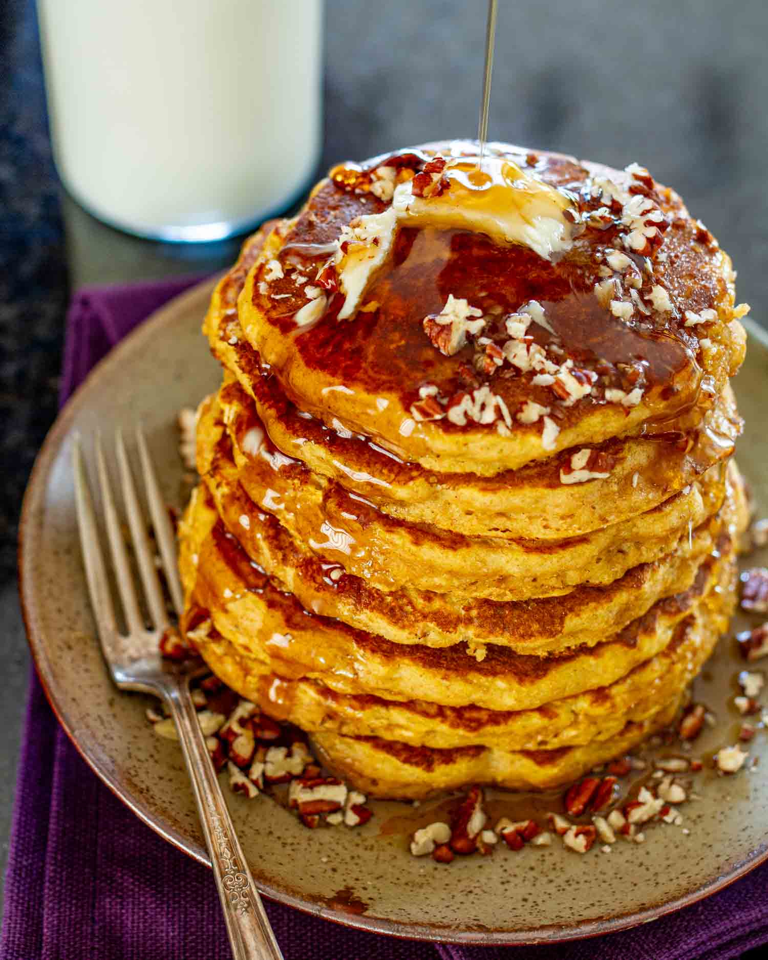 stack of whole wheat pumpkin pancakes on a plate with pecans and a pat of butter.