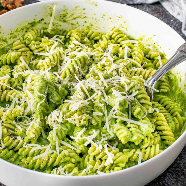 freshly made arugula walnut pesto pasta with parmesan cheese in a white bowl.