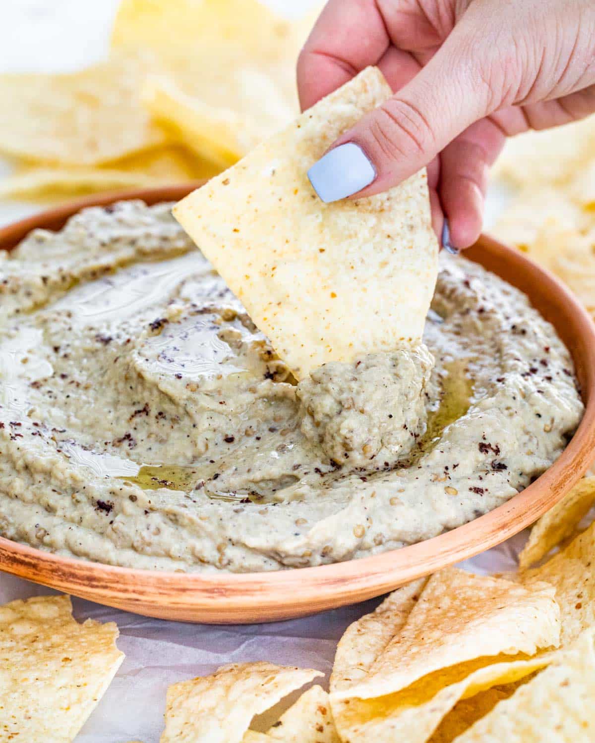 a hand dipping a chip in a bowl full of baba ganoush.