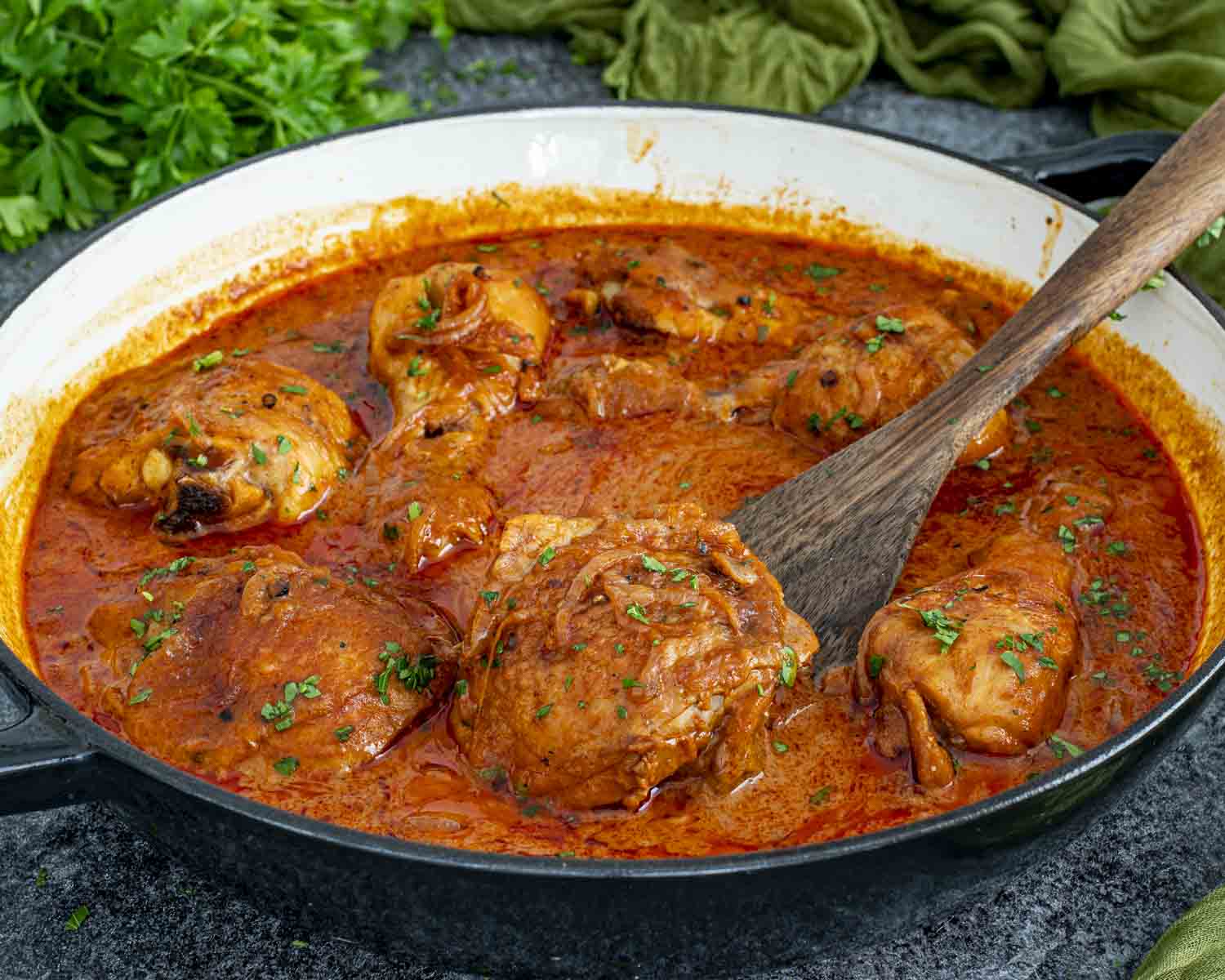 Chicken paprikash cooking in a skillet with thick paprika sauce, softened onions, and bone-in chicken.