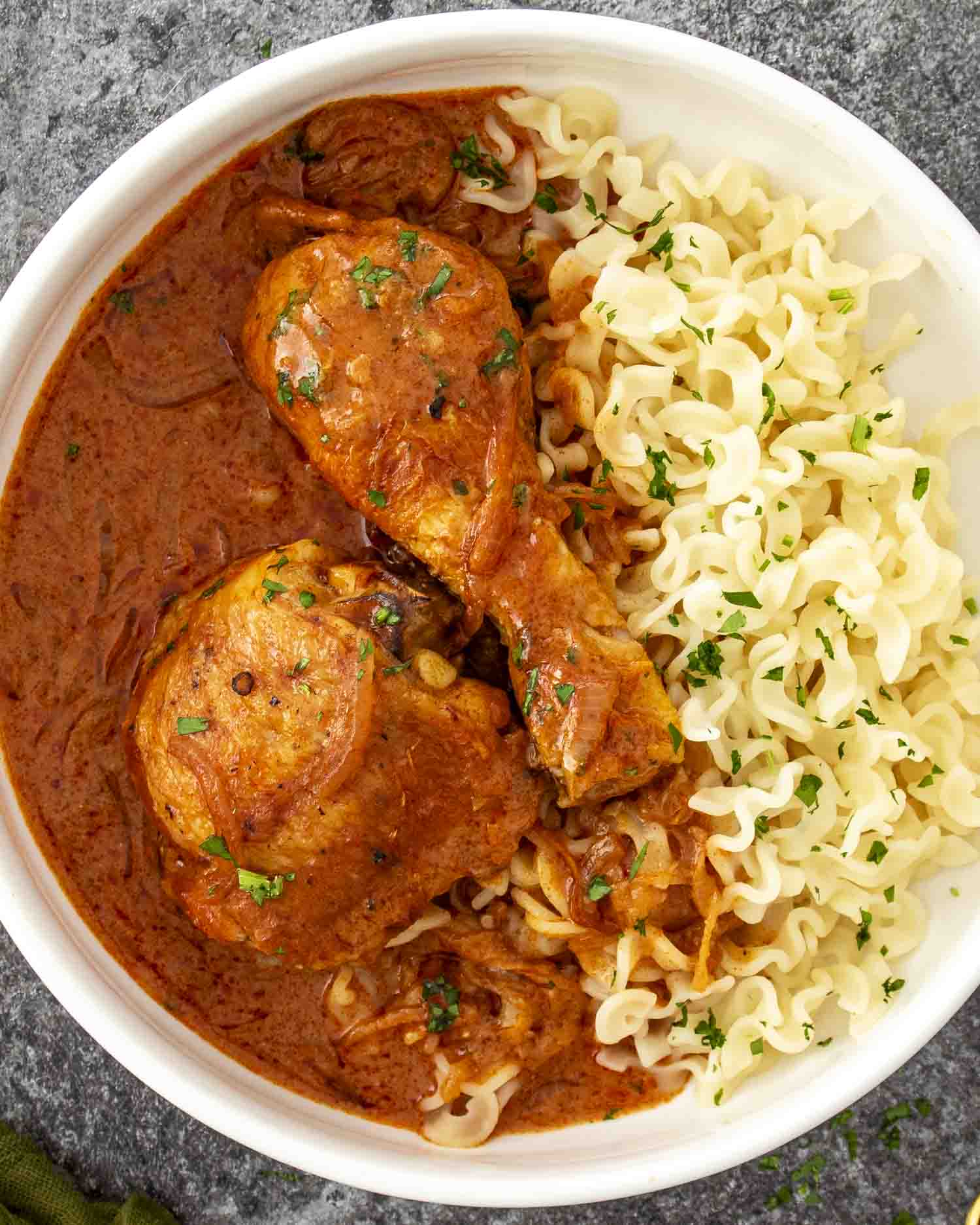 Overhead view of chicken paprikash with egg noodles and creamy paprika sauce in a white serving bowl.