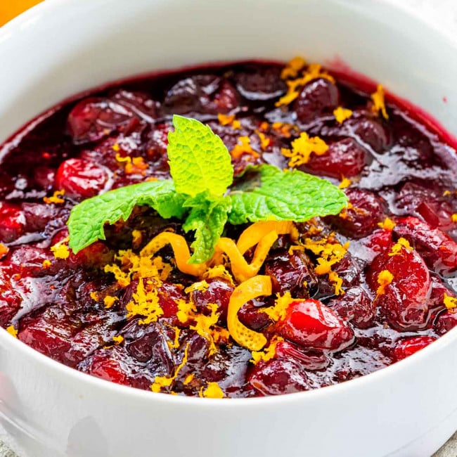 closeup of cranberry sauce in a white bowl garnished with orange zest and mint.