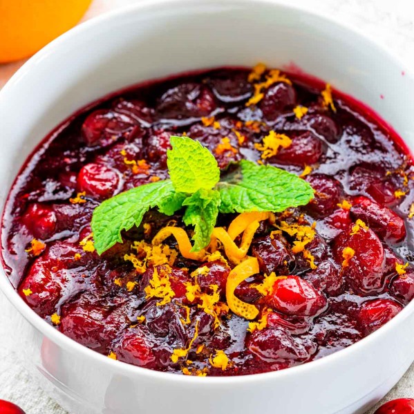 closeup of cranberry sauce in a white bowl garnished with orange zest and mint.