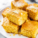 pieces of cornbread stacked on a plate with honey being drizzled over them