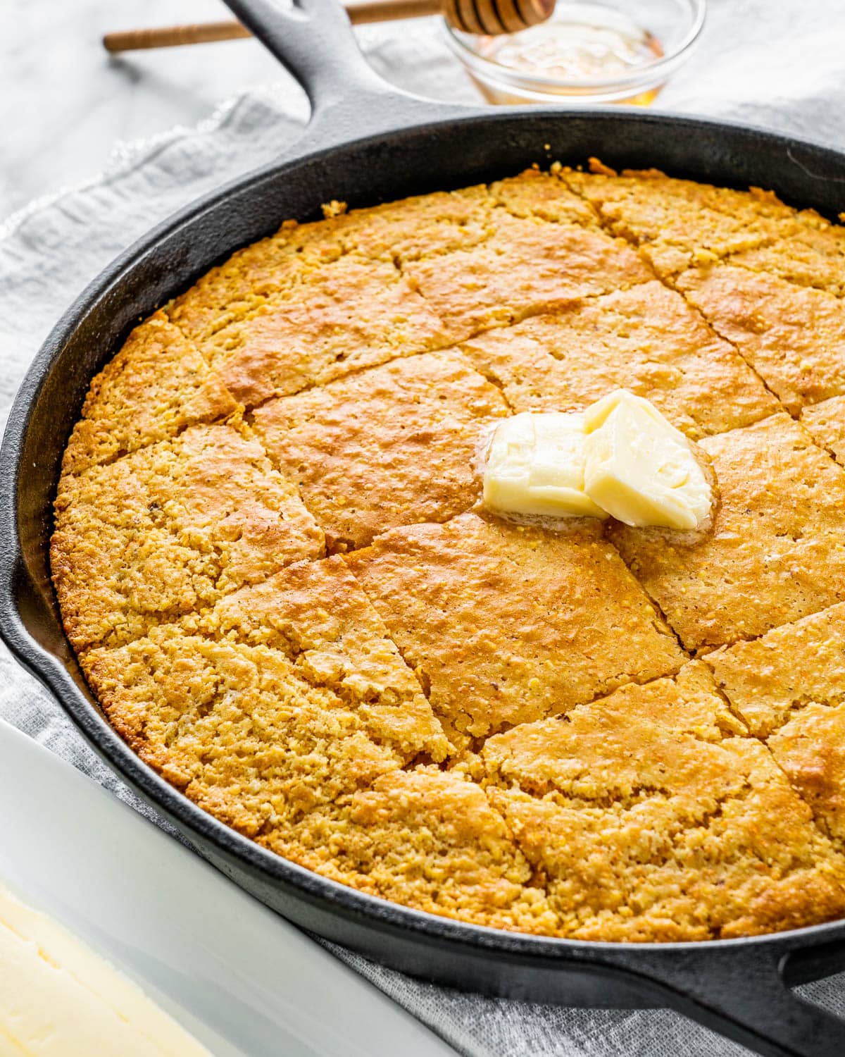 cornbread in a skillet with a couple pats of butter cut into squares