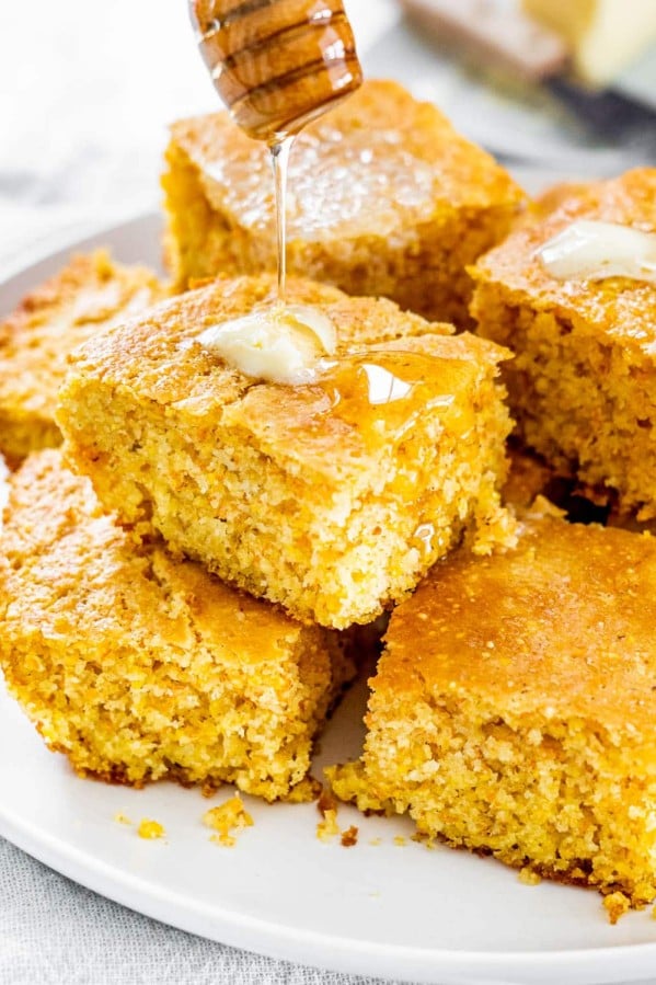 pieces of cornbread stacked on a plate with honey being drizzled over them